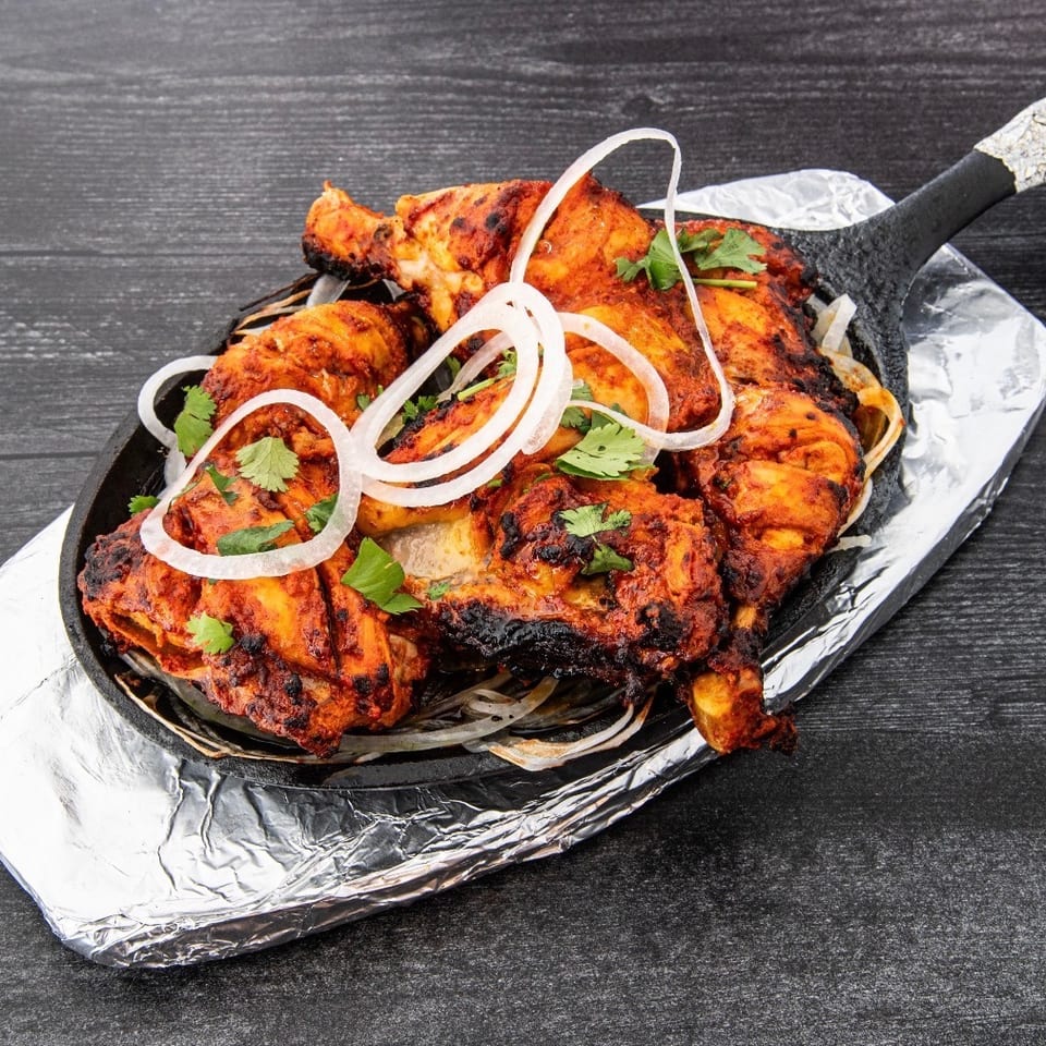 Tandoori grilled chicken pieces garnished with cilantro and onion rings, served on a foil-lined cast-iron platter.