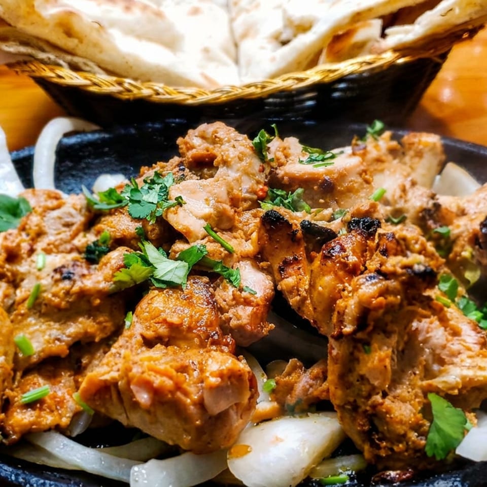 Grilled spiced chicken pieces garnished with cilantro and green onions on a black platter with sliced onions and flatbread.